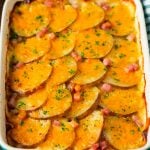 A casserole dish of scalloped potatoes and ham, topped with melted cheese and parsley.