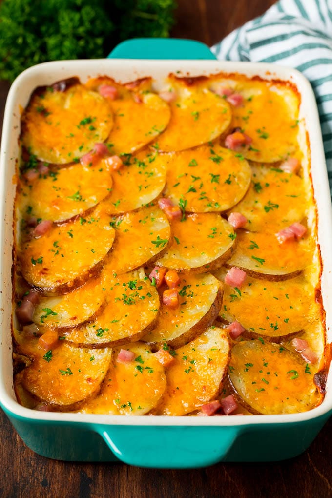 This scalloped potatoes and ham recipe is a layered casserole of thinly sliced potatoes in cheese sauce with diced ham, all baked together to golden brown perfection. A casserole dish of scalloped potatoes and ham, topped with melted cheese and parsley.