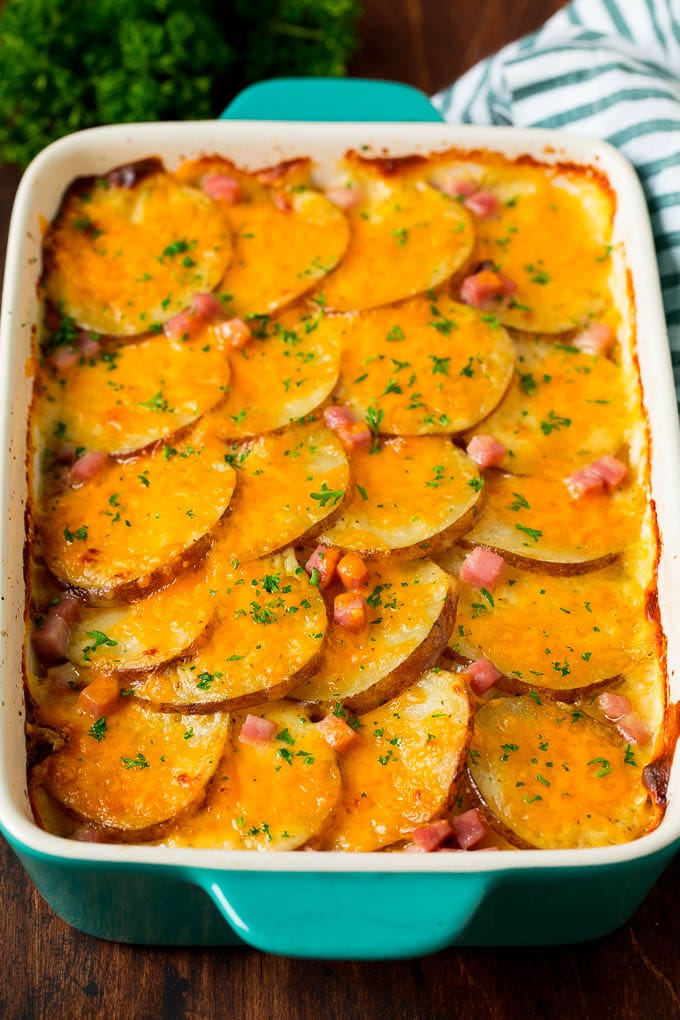 A casserole dish of scalloped potatoes and ham, topped with melted cheese and parsley.