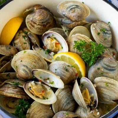 Steamed clams in a pot with lemon wedges and parsley.