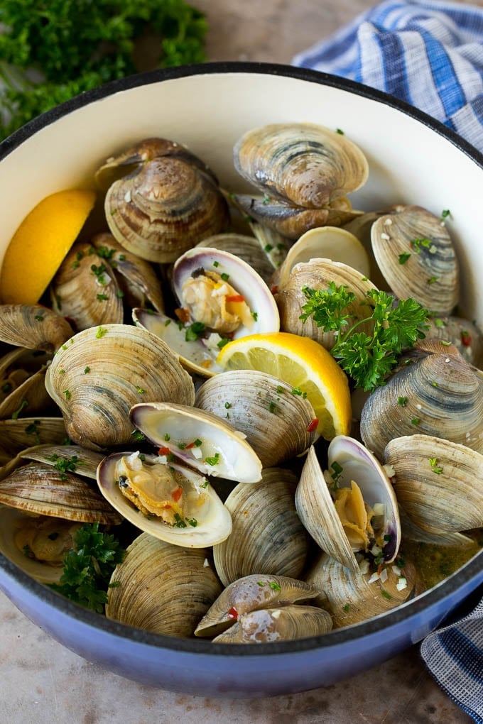 Steamed clams in a pot with lemon wedges and parsley.