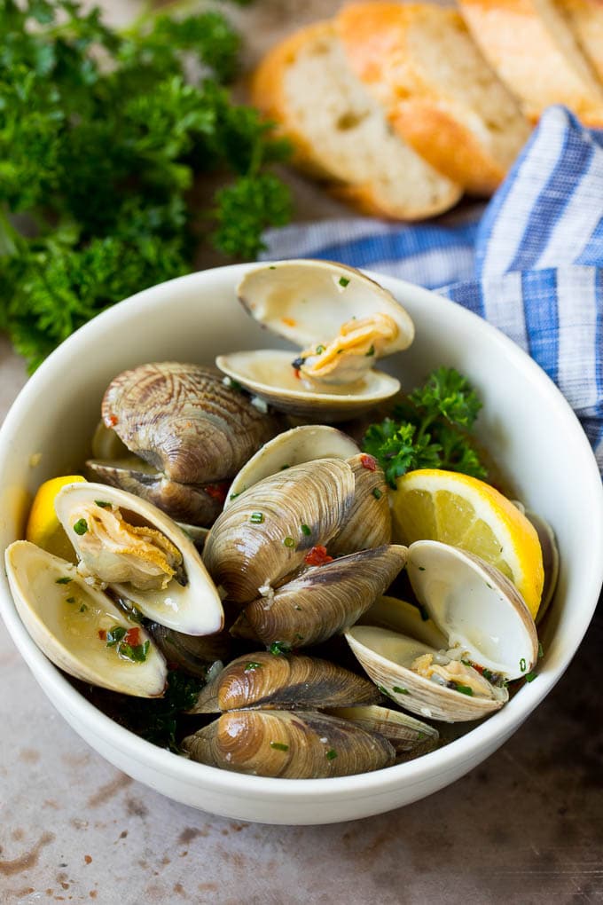 A serving bowl of steamed clams with fresh parsley and sliced bread on the side.