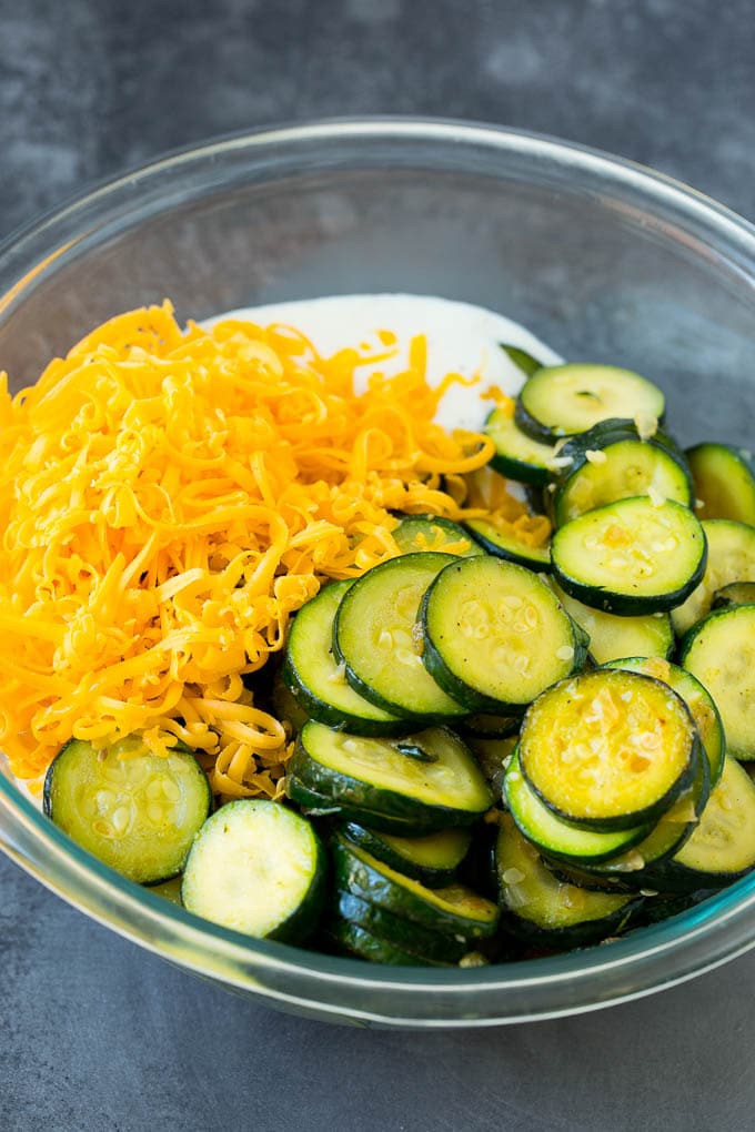 This zucchini casserole is sauteed squash tossed in a creamy sauce with plenty of cheese, all topped off with cracker crumbs and baked to perfection. Zucchini, cheese and sauce in a bowl.
