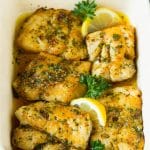 A pan of baked cod garnished with lemon and parsley.
