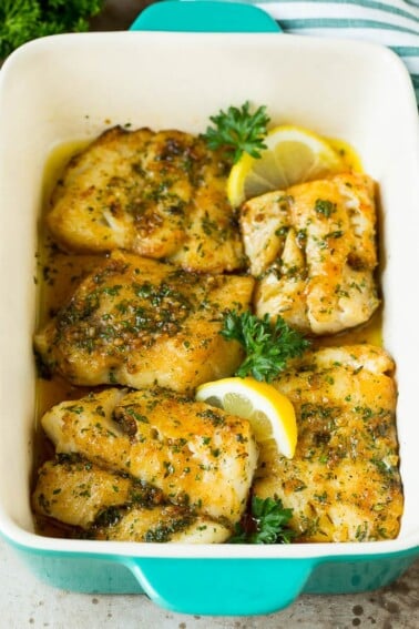 A pan of baked cod garnished with lemon and parsley.