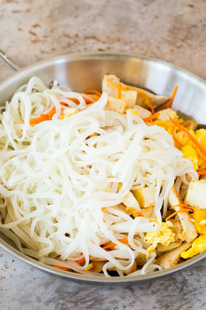 Rice noodles in a pan with eggs, carrots, chicken and tofu.