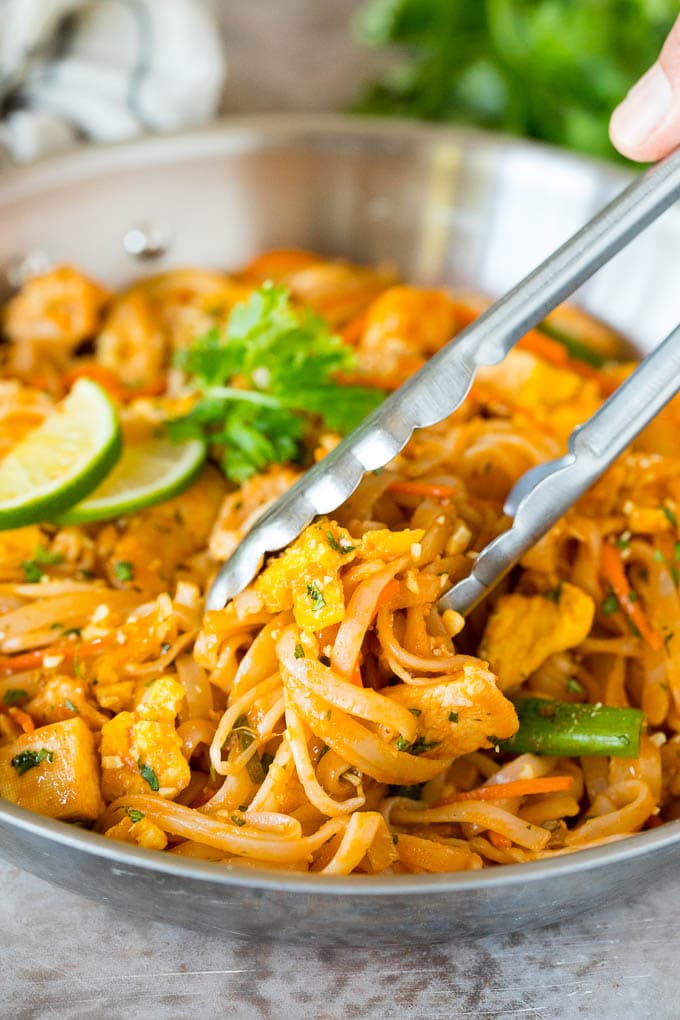 Tongs serving up a portion of chicken pad thai.