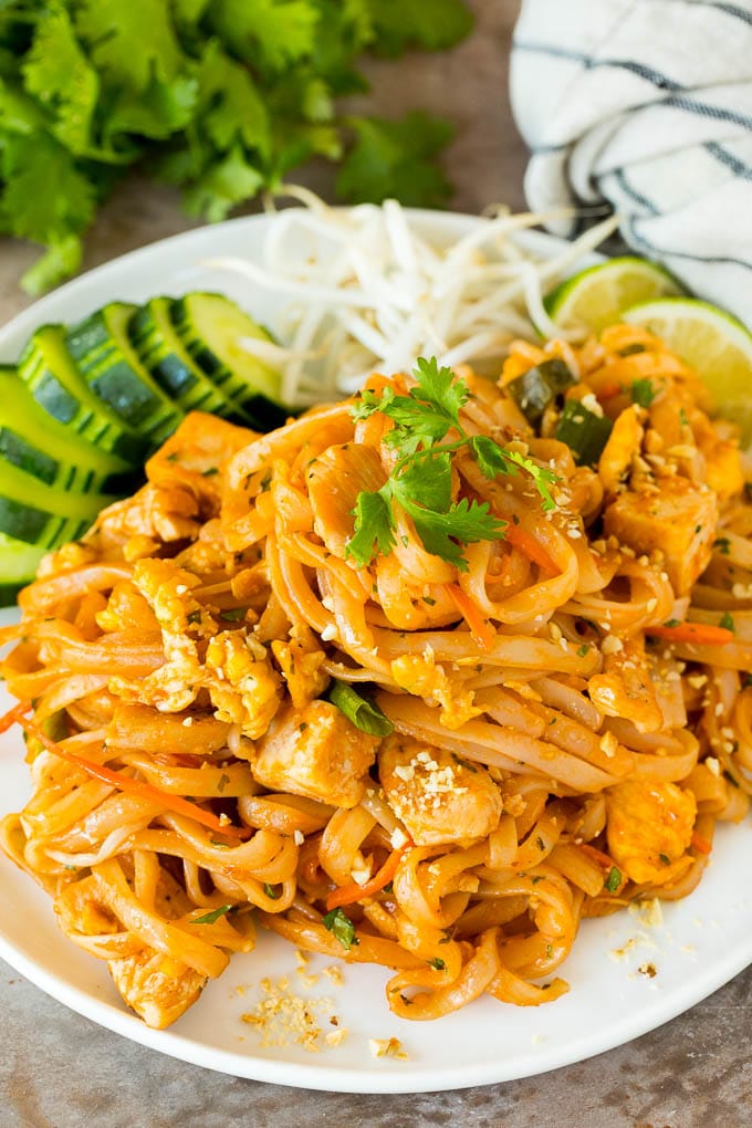 A plate of chicken pad thai served with bean sprouts and cucumber.