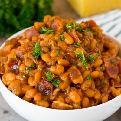 A bowl of cowboy beans topped with parsley and served with cornbread.