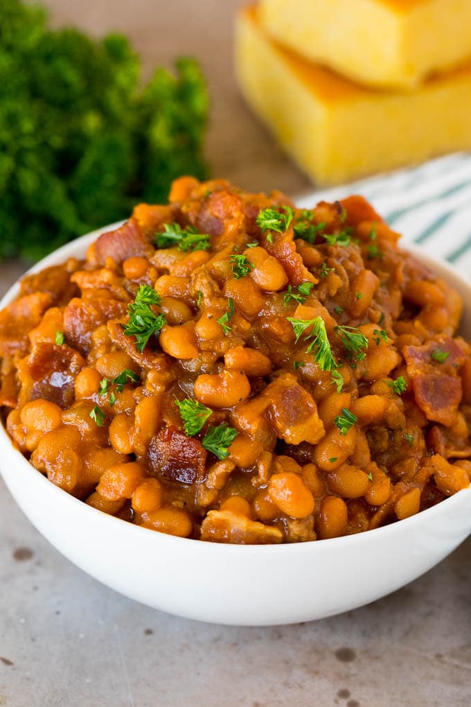 A bowl of cowboy beans topped with parsley and served with cornbread.
