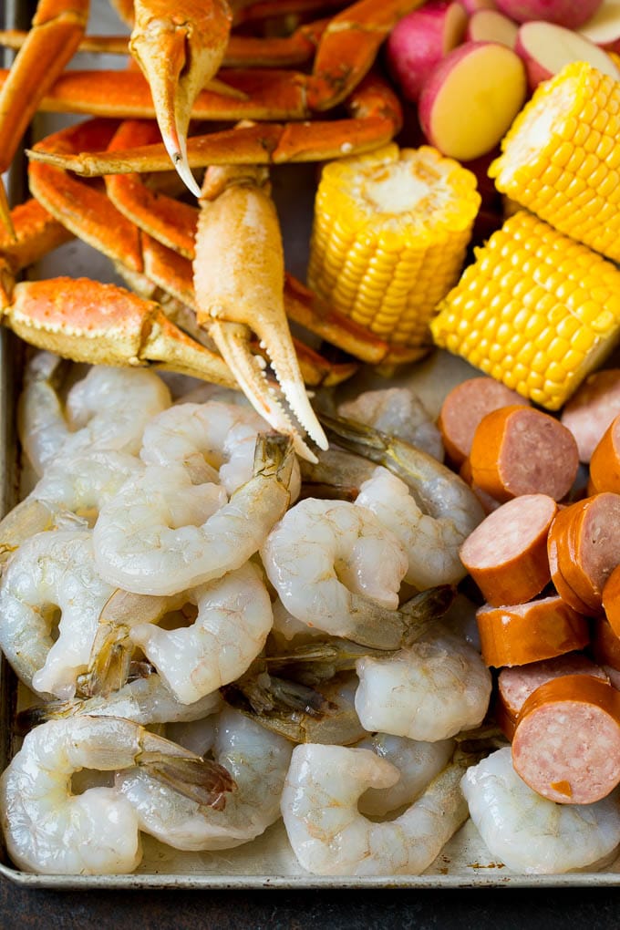 Shrimp, sliced sausage, crab legs and corn cobs on a sheet pan.