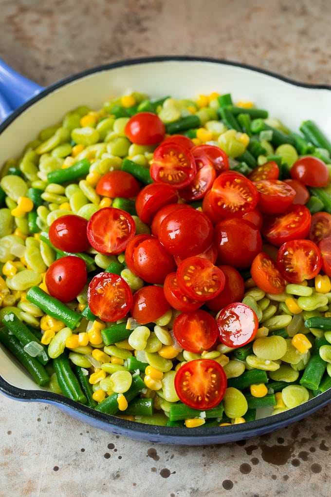 A pile of cherry tomatoes on top of a mixture of corn and beans.