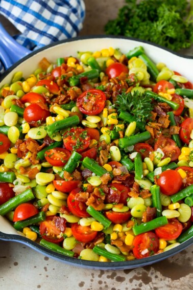 A skillet of succotash topped with bacon and herbs.