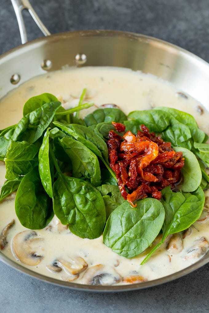 A pan of creamy mushroom sauce with spinach and sun dried tomatoes.