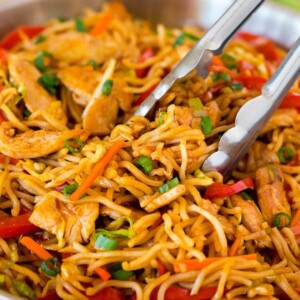 Tongs serving up a portion of yakisoba noodles with vegetables and chicken.