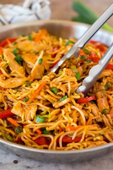 Tongs serving up a portion of yakisoba noodles with vegetables and chicken.