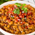 A bowl of charro beans topped with bacon and pico de gallo.