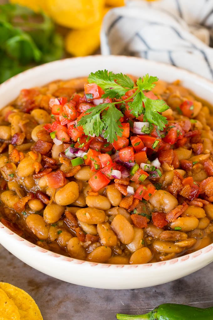 A bowl of charro beans topped with bacon and pico de gallo.