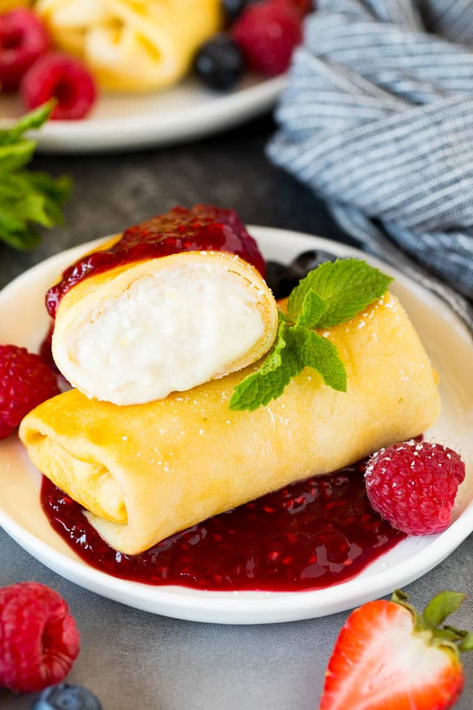 A plate of cheese blintzes with raspberry sauce and fresh fruit.