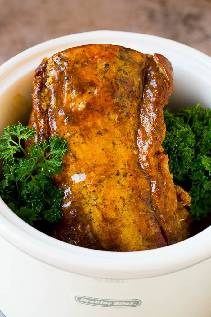 Crock pot pork roast inside a slow coker with gravy, garnished with parsley.