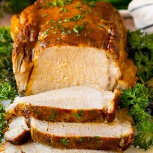 Crock pot pork loin sliced on a serving plate, garnished with herbs.