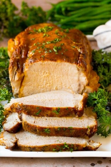 Crock pot pork loin sliced on a serving plate, garnished with herbs.