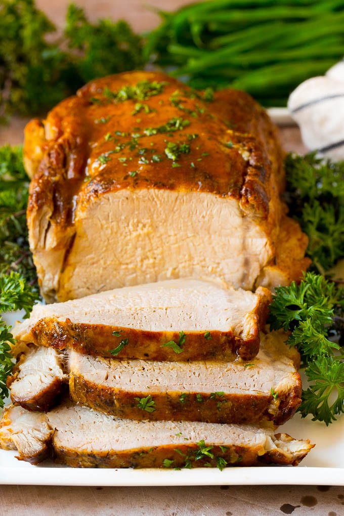 Crock pot pork roast sliced on a serving plate, garnished with herbs.