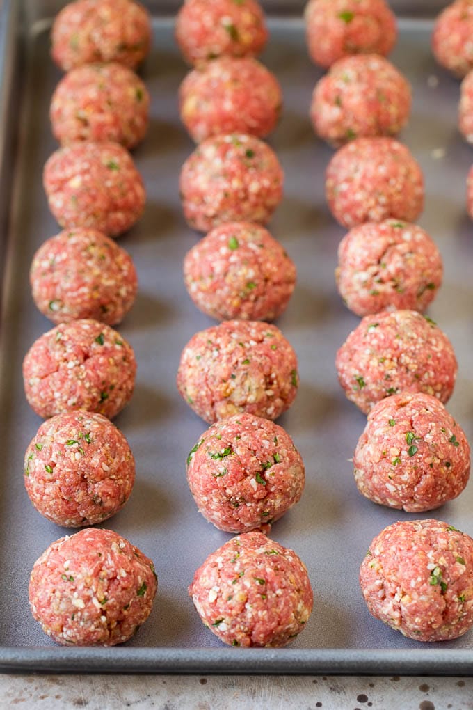 Meatballs lined up on a sheet pan.