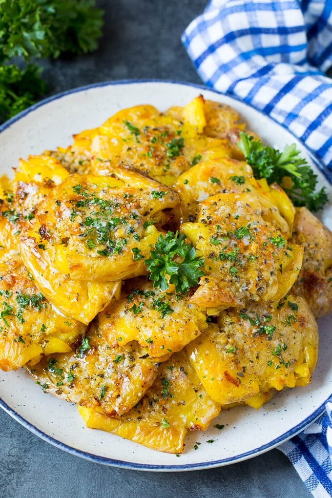 A serving plate of smashed potatoes garnished with parsley.