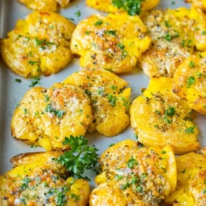 Smashed potatoes on a sheet pan, topped with garlic butter and parsley.