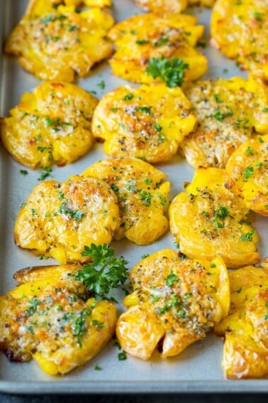 Smashed potatoes on a sheet pan, topped with garlic butter and parsley.