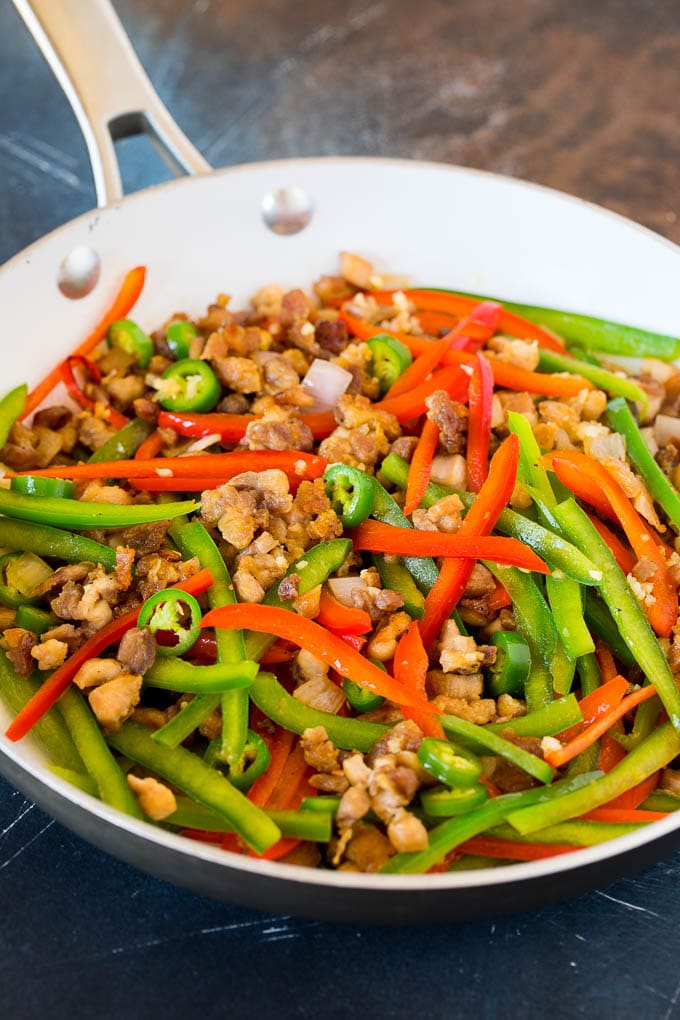 Chicken with bell peppers, serrano chilies and garlic in a pan.