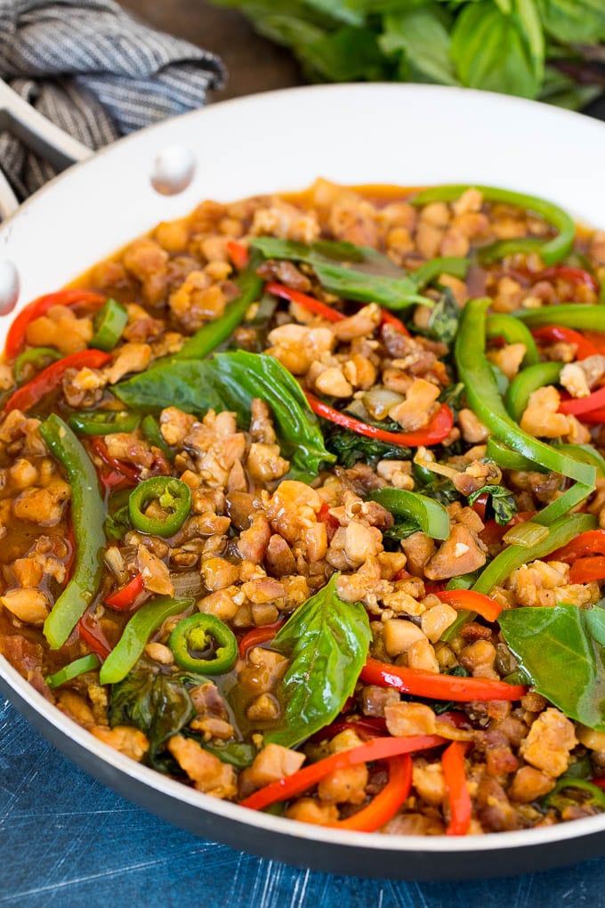 A pan of Thai basil chicken with peppers and fresh basil leaves.