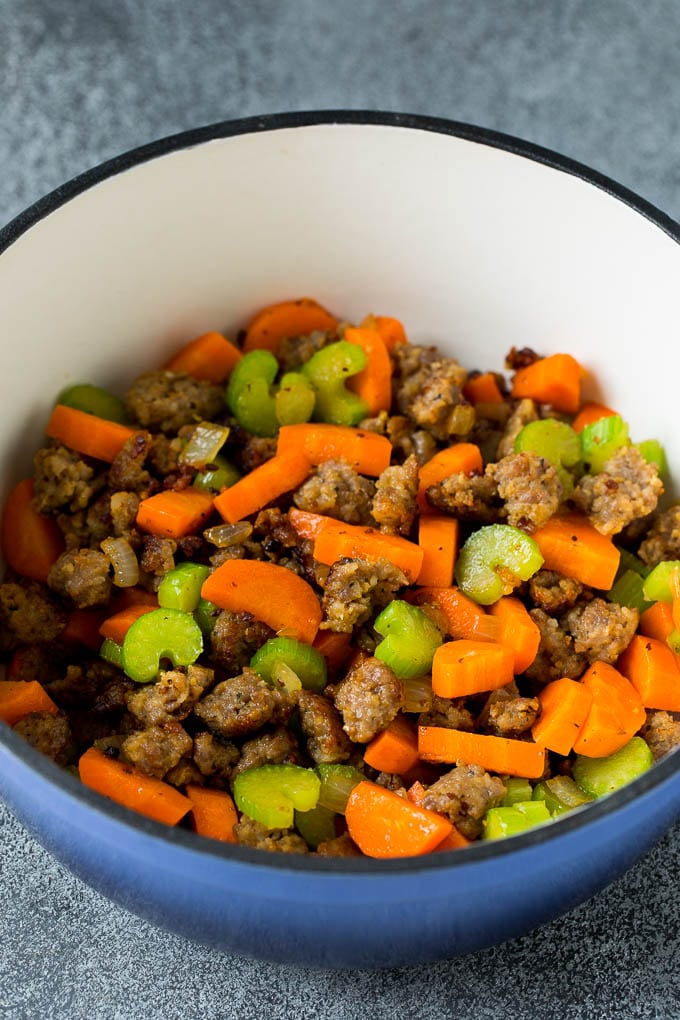 This Tuscan white bean soup is a hearty blend of Italian sausage, vegetables and beans, all simmered together in a savory tomato broth. Sausage, carrots and celery in a soup pot.