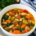 A bowl of white bean soup with Italian sausage, tomatoes and spinach.