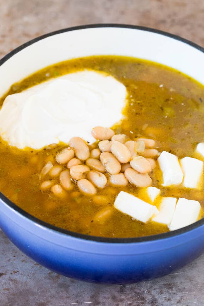 This white chicken chili is a creamy blend of chicken, chilies, beans and spices, all simmered together A pot of broth and chicken with beans, sour cream and cream cheese.