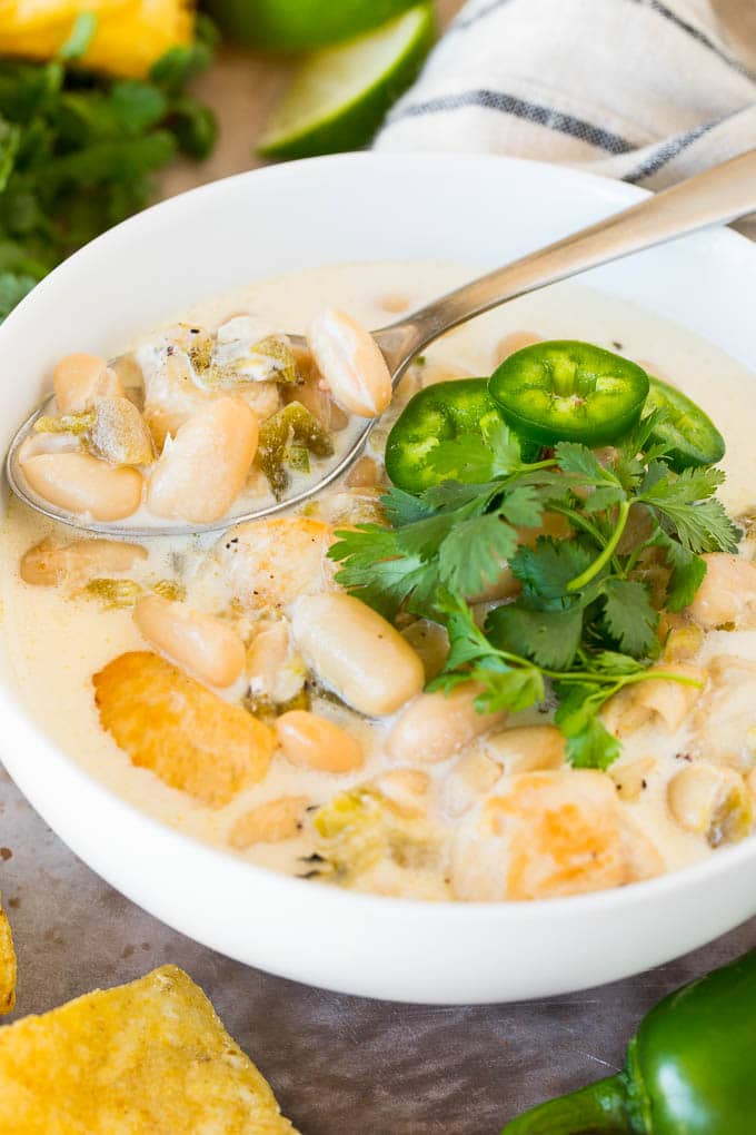 This white chicken chili is a creamy blend of chicken, chilies, beans and spices, all simmered together A bowl of white chicken chili with a spoon in it.