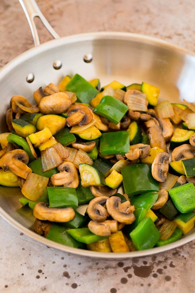 This almond chicken is a stir fry of chicken thigh pieces, assorted vegetables and crunchy almonds, all tossed in a savory sauce. Mushrooms, zucchini and bell peppers cooked in a pan.