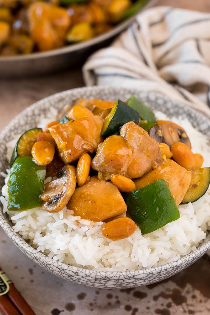 This almond chicken is a stir fry of chicken thigh pieces, assorted vegetables and crunchy almonds, all tossed in a savory sauce. Almond chicken served over steamed rice in a bowl.