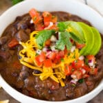 A bowl of black bean soup topped with salsa, avocado and cheese.