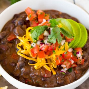 A bowl of black bean soup topped with salsa, avocado and cheese.