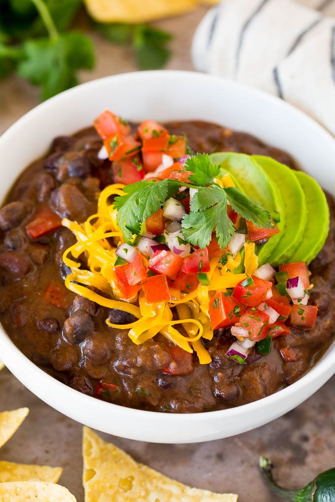 This black bean soup is a zesty blend of beans and vegetables, simmered together to make a thick and hearty meal. Add your favorite toppings and you'll have an easy and healthy dinner option that's sure to get rave reviews! A bowl of black bean soup topped with salsa, avocado and cheese.