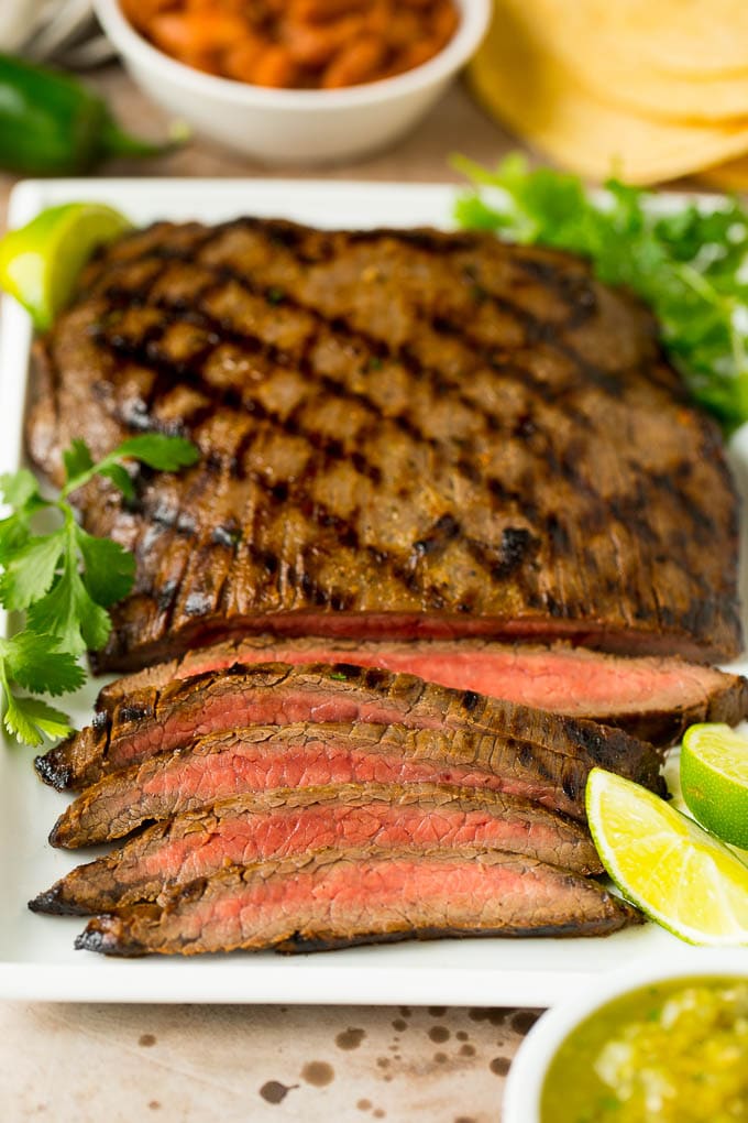 Sliced flank steak garnished with cilantro and limes.