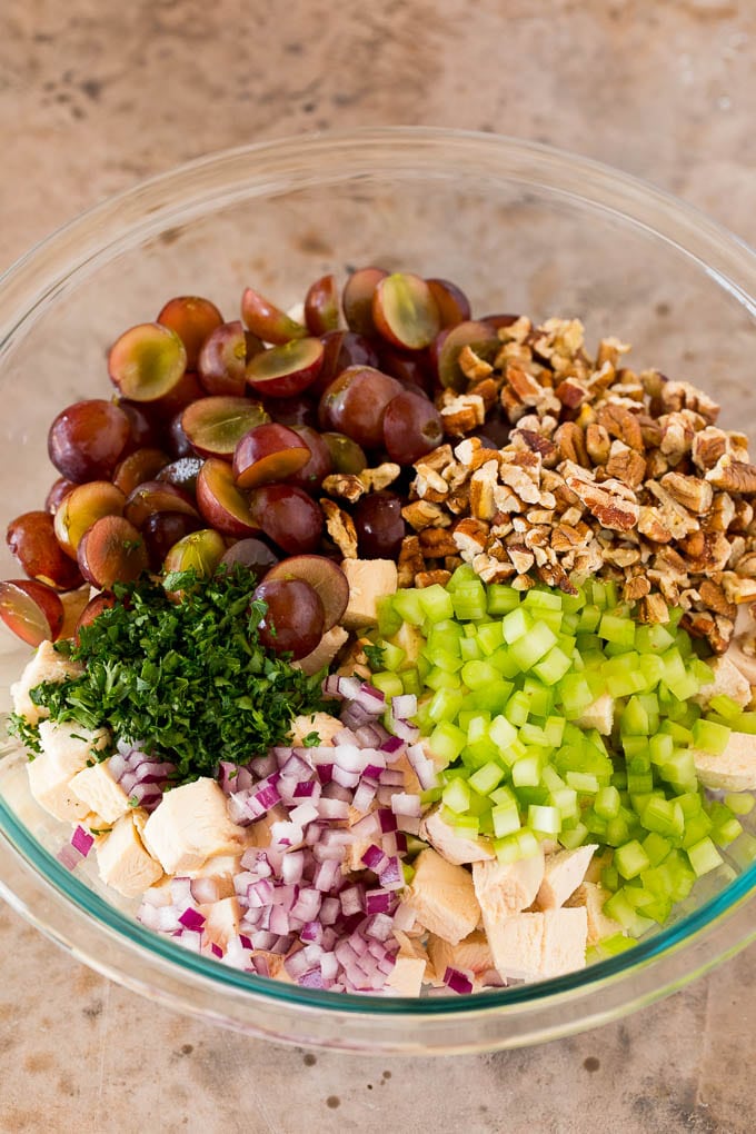 A mixing bowl with chicken, grapes, pecans and red onions.