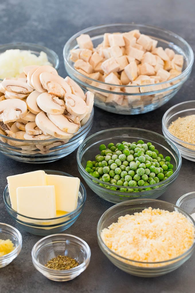 Ingredients in bowls including chicken, peas, mushrooms, cheese and seasonings.