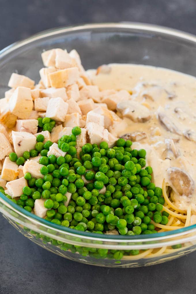 Spaghetti, peas, chicken and mushroom sauce in a bowl.