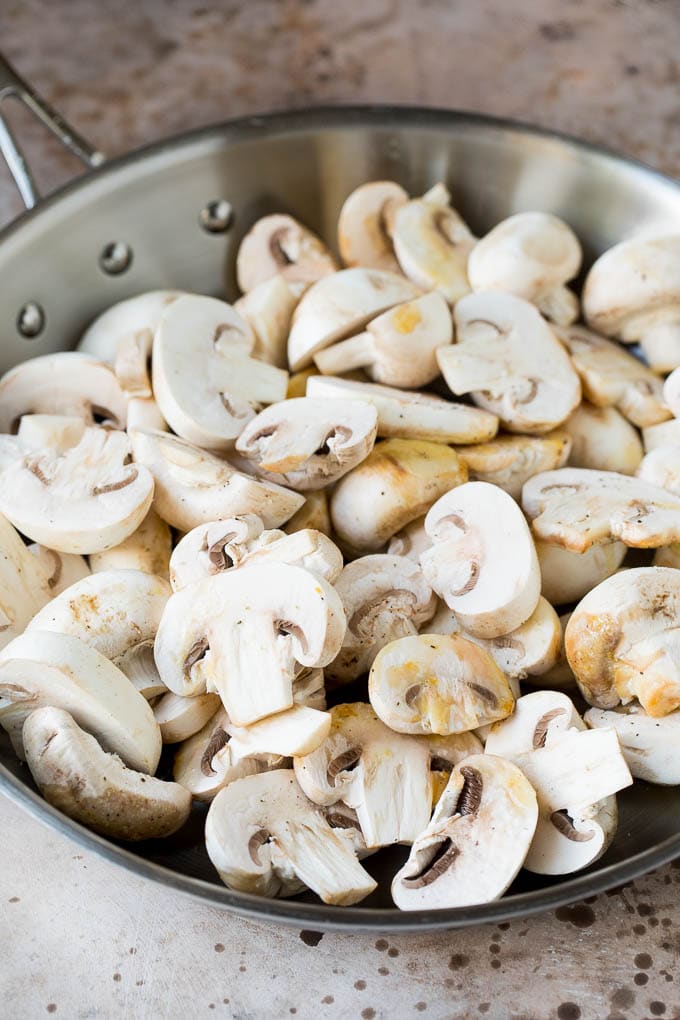 Raw sliced mushrooms in a skillet.