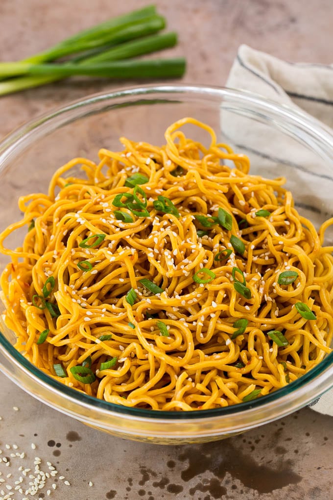 A bowl of sesame noodles garnished with sesame seeds and green onions.