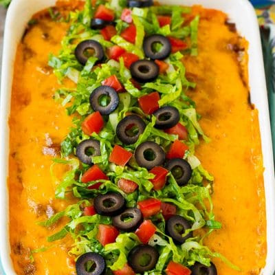 Taco bake topped with melted cheese, lettuce, tomatoes and olives.