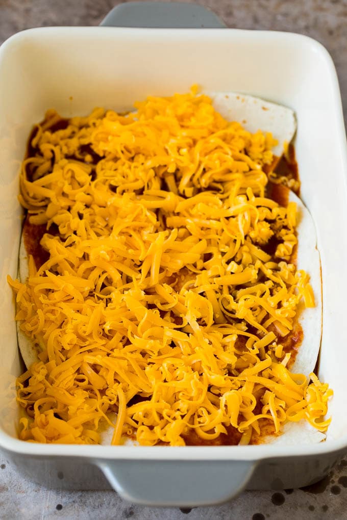 Layers of tortillas, cheese and enchilada sauce in a baking dish.